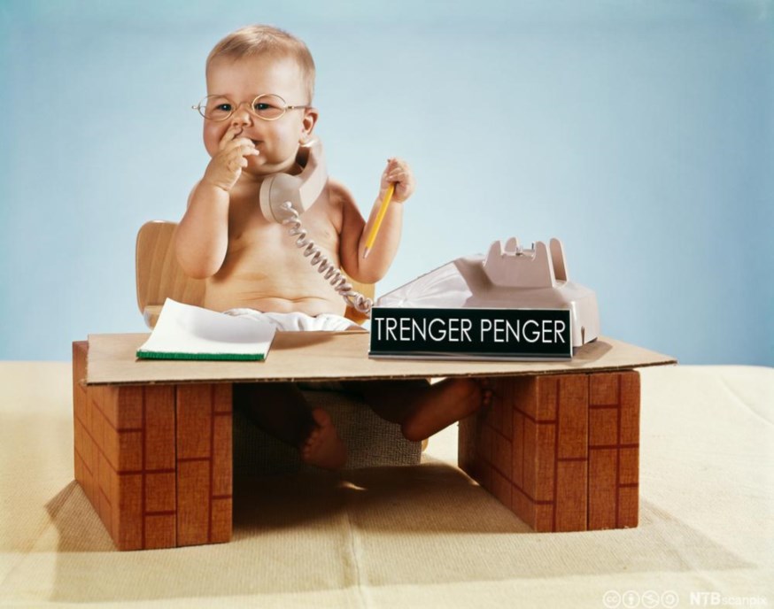 Liten gutt bak en kontorpult med tekst: Trenger penger